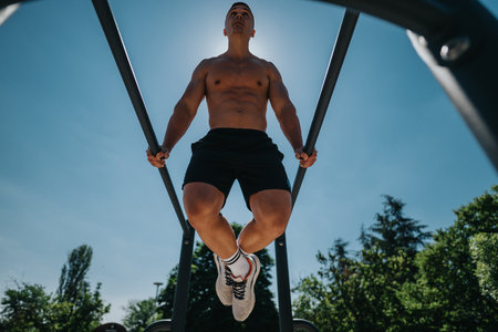 Athletic man exercising on parallel bars in outdoor park under sunny skiesの写真素材