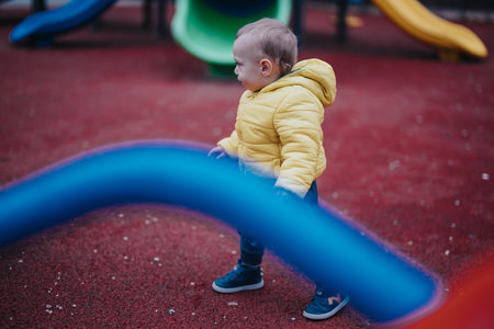 Child in a yellow jacket playing at a vibrant outdoor playgroundの写真素材