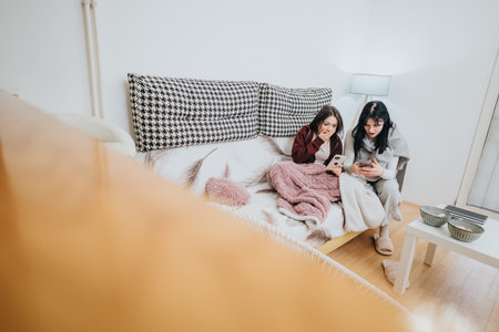 Two girls sitting on couch at home using mobile devicesの写真素材