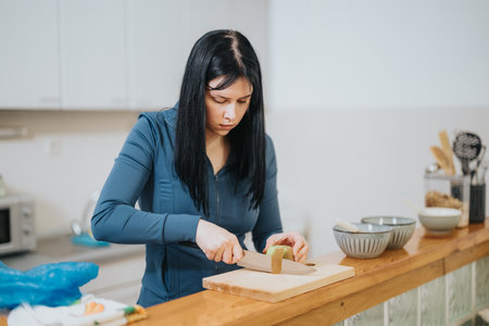 Young woman carefully chopping vegetables while preparing a meal in the kitchenの写真素材