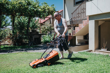 Man mowing the lawn in a sunny backyard with an orange mower near a house, showing outdoor yard work and home maintenanceの写真素材