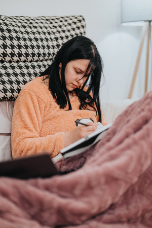 Young woman writing while relaxing at home on a cozy seating arrangementの写真素材