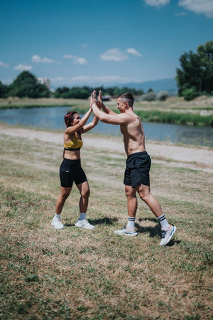 Two fitness enthusiasts enjoying outdoor exercise with a high five by a riverの写真素材