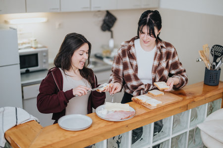 Two young women making sandwiches and enjoying time together in their kitchenの写真素材