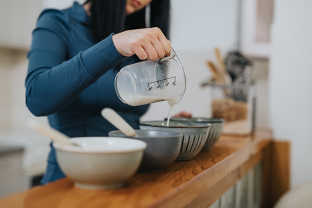 Woman pouring liquid into bowls at home while preparing a mealの写真素材