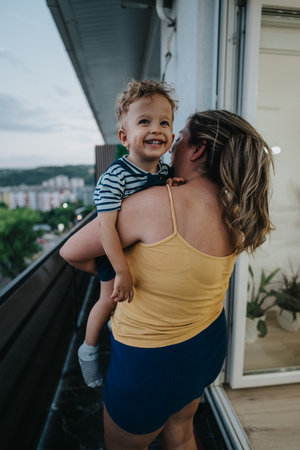 Mother and toddler on balcony smiling together, enjoying a sunny moment above the cityの写真素材