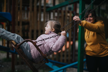 Mother pushes her daughter on a swing in a park playground