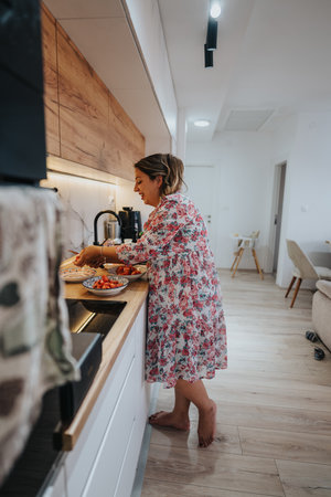 Woman in floral dress preparing fruit bowls in a modern home kitchenの写真素材