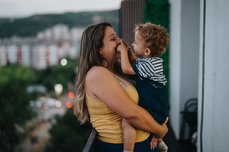 Loving mother holds toddler on balcony with city view, capturing a warm family momentの写真素材