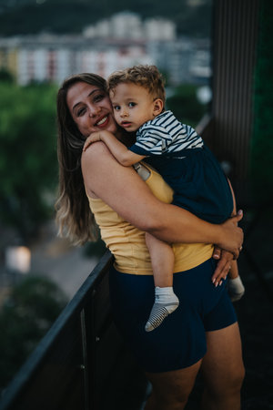 Mother holds laughing child on balcony in urban setting, a warm moment of love and connectionの写真素材