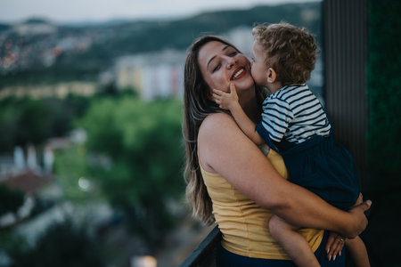 A loving mother holds her child in a warm embrace with a distant city view and sunny sky