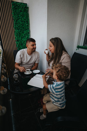 Family and friends share coffee on a balcony, chatting as a child draws in a notebookの写真素材