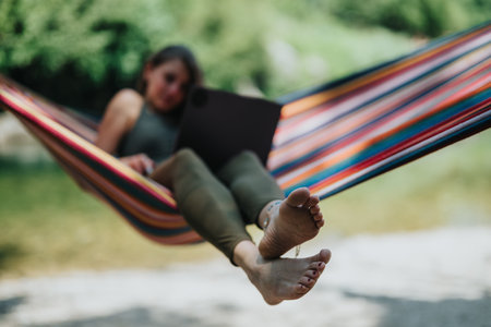 Woman using laptop while relaxing in a colorful hammock outdoorsの写真素材