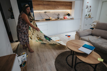 Woman folding a large rug in a modern, cozy living room at homeの写真素材