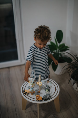 Young boy plays with wooden train set on a small round table indoorsの写真素材