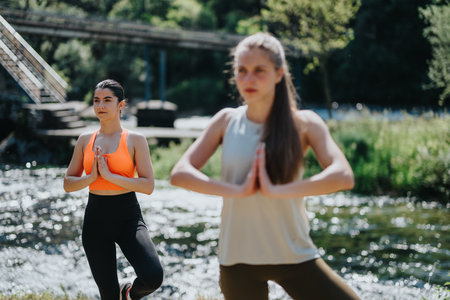 Two women practicing yoga by a tranquil river in natural surroundingsの写真素材