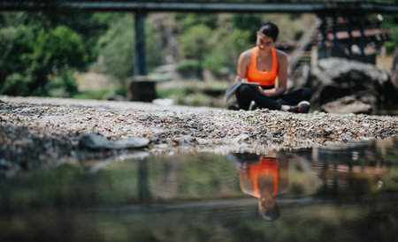 Woman sitting near a river reflecting on the peaceful natural surroundingsの写真素材
