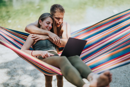 Couple working remotely on a laptop while relaxing together in a hammock outdoorsの写真素材
