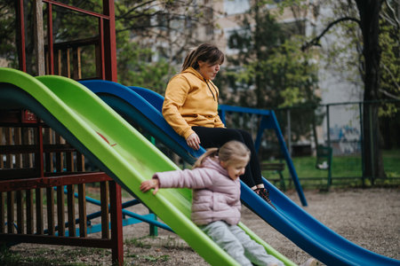 Mother and young daughter enjoying fresh air on playground slides in parkの写真素材