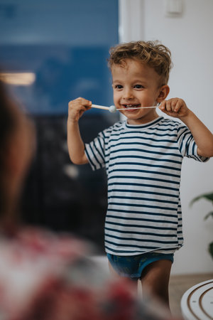 Happy toddler in striped shirt enjoys a playful moment with a spoon indoors at homeの写真素材