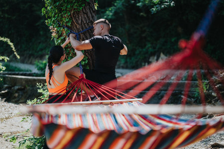 Couple setting up a colorful hammock in a serene outdoor forest locationの写真素材