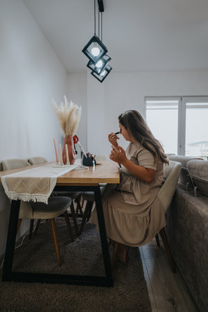 Woman applying makeup at a dining table in a modern living room with pendant lights and decorative vaseの写真素材