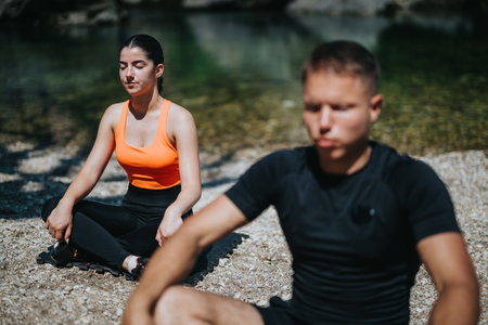 Two individuals meditating outdoors near a serene natural water bodyの写真素材