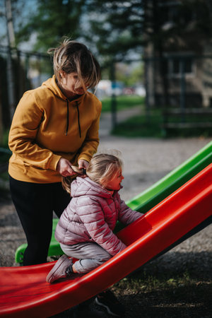 Mother helping daughter climb slide at the park on a sunny dayの写真素材