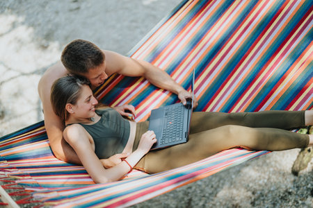 Couple working remotely on laptop while relaxing in colorful outdoor hammock