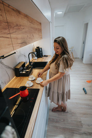 Woman preparing coffee in a modern kitchen, placing cups on the wooden countertop for guestsの写真素材