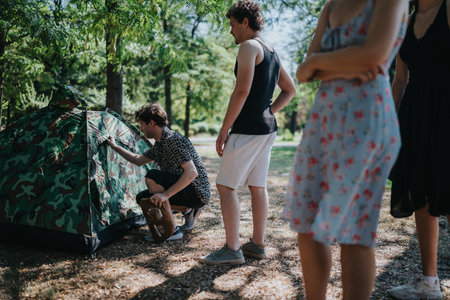 Friends prepare a camouflage tent during a sunny outdoor camping trip in a park.の写真素材
