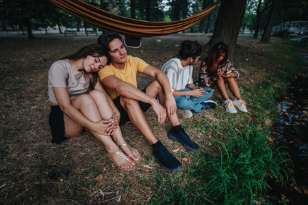 Friends relaxing by the park riverbank in a hammock, enjoying a calm afternoon togetherの写真素材