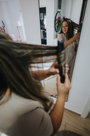 Woman brushing long hair in front of mirror in stylish bedroom during morning routineの写真素材