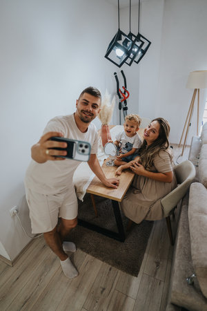Family selfie at home: mom, dad, and child share a joyful moment in a cozy living roomの写真素材
