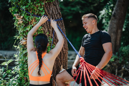 Two friends setting up a hammock together in a forest area