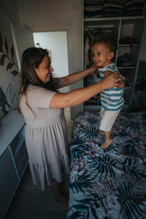 Joyful mother lifts smiling toddler on bed in cozy bedroom during playtimeの写真素材