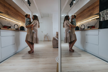 Mother holds child in a modern kitchen, mirrored image creates a warm, loving family moment.の写真素材