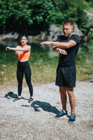 Two individuals performing yoga stretches outdoors near a serene riverside settingの写真素材