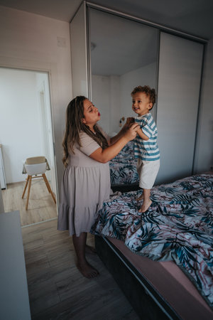 Mother and excited little boy share a joyful moment on the bed at homeの写真素材