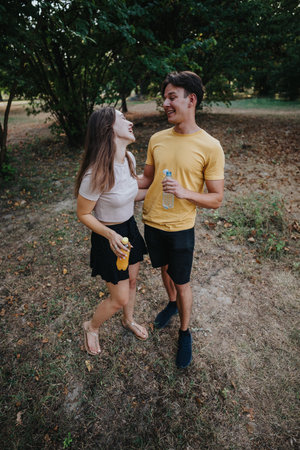 Happy couple enjoys outdoor date in park, sharing drinks and laughing togetherの写真素材