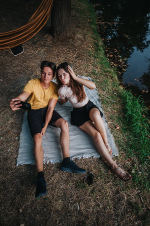 Couple enjoying a relaxing selfie on a mat by the lake during a casual outdoor momentの写真素材
