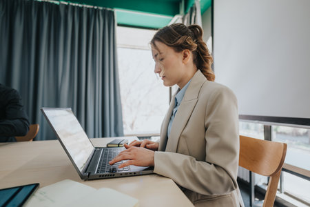 Woman working on a laptop computer in a modern office settingの写真素材
