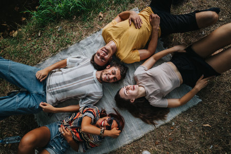 Group of friends lying on a blanket outdoors, smiling and enjoying a casual, relaxed moment togetherの写真素材