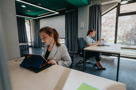 Two businesswomen working on tablets and documents in a modern office spaceの写真素材
