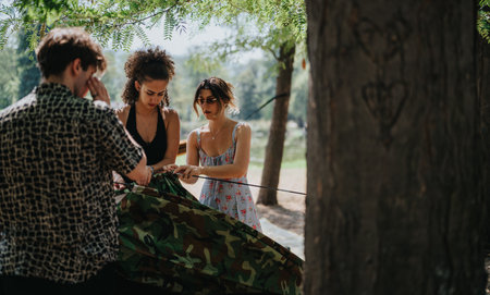 Friends set up camouflage tent in a sunny park, enjoying outdoor camping and teamworkの写真素材
