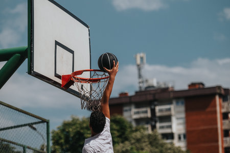 Young athlete dunks basketball on an outdoor court under a clear blue skyの写真素材