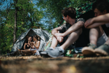 Friends enjoy a sunny forest campsite chat near a tent during a fun outdoor camping tripの写真素材