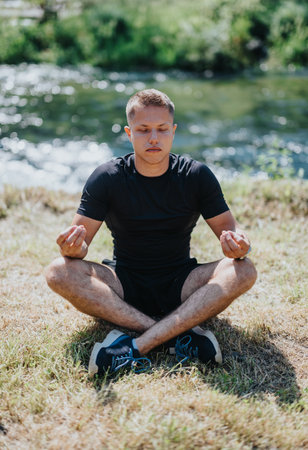 Man practicing meditation by a river in a peaceful natural settingの写真素材