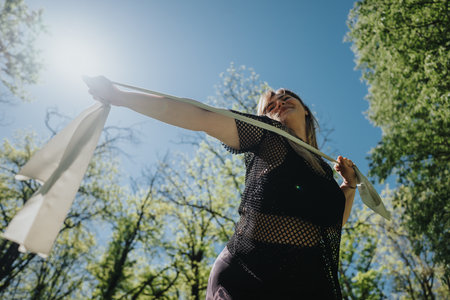 Woman enjoying a sunny day outdoors surrounded by lush greenery, expressing freedom and joy with a...