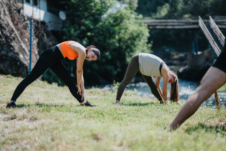 People practicing yoga stretches on a grass lawn near a serene river.の写真素材